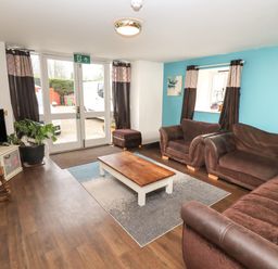 A living room with brown sofas a wooden coffee table and double glass doors at Greyhound Barn Barnsley near Cirencester
