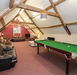 A game room with a billiard table and multiple sofas under exposed wooden beams at Greyhound Barn Barnsley near Cirencester