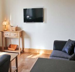 A living room with a wall mounted TV a wooden side table with baskets a lamp and two sofas at Moat Farm Cottage in Wood Dalling