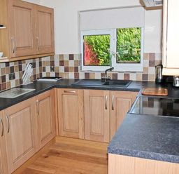 A kitchen with wooden cabinets black countertops a window and tiled backsplash at Moat Farm Cottage in Wood Dalling
