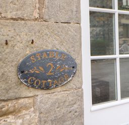 A close up of a sign on a stone wall next to a white window at Stable Cottage in Belford near Bamburgh