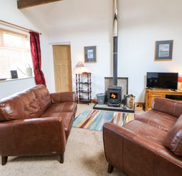A living room with two brown leather sofas a wood burning stove colorful rug and a television at Stable Cottage Belford near Bamburgh