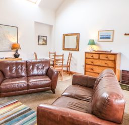 A living room with two brown leather sofas a striped rug a wooden dresser and a dining table at Stable Cottage in Belford near Bamburgh