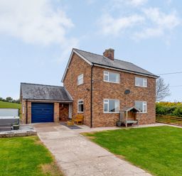 A brick house with a driveway garage and a wooden bench near the entrance at Pen Y Gaer in Llannefydd near Abergele and Denbigh