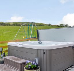 An outdoor hot tub with steps and flower pots next to a swing set in a grassy field at Pen Y Gaer in Llannefydd near Abergele and Denbigh