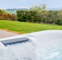 A hot tub with water flowing into it in a garden with grass and hedges at Pen Y Gaer in Llannefydd near Abergele and Denbigh