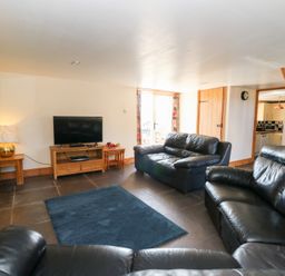A living room with black leather sofas a television on a wooden stand and a wooden staircase at Mill Cottage in Aberaeron