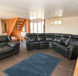 A living room with black leather sofas wooden staircase and blue rug at Mill Cottage in Aberaeron