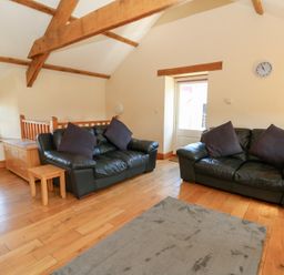 A living room with two black leather sofas with dark cushions wooden floor and exposed wooden ceiling beams at The Stable in Aberaeron