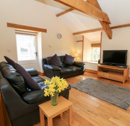 A living room with leather sofas a television a wooden table with flowers and wooden beams at The Stable in Aberaeron