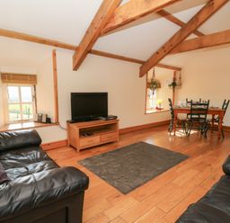 A living room with leather sofas a television on a wooden stand a dining table with chairs and exposed wooden ceiling beams at The Stable in Aberaeron