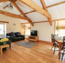A living room with wooden beams on the ceiling two black leather sofas a wooden dining table with chairs and a television on a wooden stand at The Stable in Aberaeron