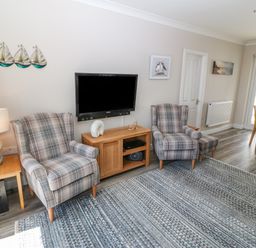 A living room with two plaid armchairs a wall-mounted television and a wooden side table at St Winifreds in Rhosneigr