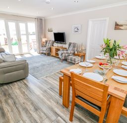 A living room with a sofa chairs a wooden dining table set with plates glasses and flowers at St Winifreds in Rhosneigr