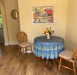 A small dining area with a round table covered by a blue tablecloth and two wooden chairs with cushions at Oke Apple Cottage in Okeford Fitzpaine