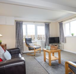 A living room with two gray armchairs a dark sofa a wooden coffee table and a television at Glan Y Don Bach in Abersoch