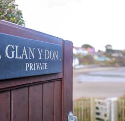 A wooden gate with a sign reading Glan Y Don Private with a beach and houses visible in the background at Glan Y Don Bach in Abersoch