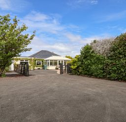 A house with a conservatory and driveway surrounded by trees and bushes at Beach Cottage in Conwy