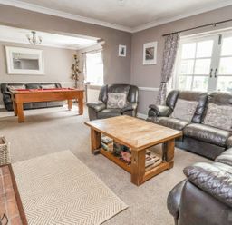 A living room with leather sofas a wooden coffee table a pool table and a fireplace at Beach Cottage in Conwy
