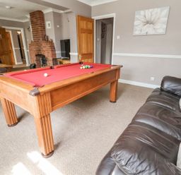 A living room with a red pool table a brown leather sofa a brick fireplace and a television at Beach Cottage in Conwy