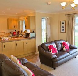 A living room area with two leather sofas with floral cushions next to a kitchen with wooden cabinets at Sunrise Kessingland near Lowestoft