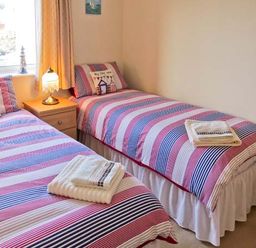 A bedroom with two single beds with striped bedding and a bedside table with a lamp at Sunrise in Kessingland near Lowestoft