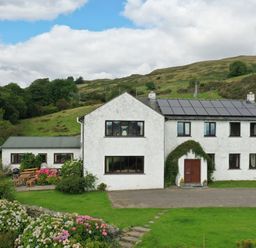 A white house with solar panels on the roof surrounded by a garden and hills at Ghyll Bank House in Staveley near Windermere
