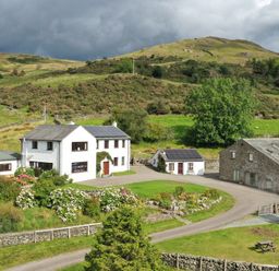 A farmhouse and outbuildings with garden and hills in the background at Ghyll Bank House in Staveley near Windermere