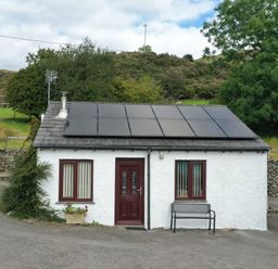 A small white house with solar panels on the roof a red door and two windows with vertical blinds at Ghyll Bank Bungalow in Staveley near Windermere