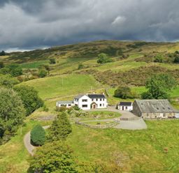 A farmhouse and barn on a hillside with green fields and trees at Ghyll Bank Bungalow in Staveley near Windermere