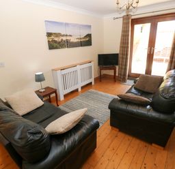 A living room with two sofas, a television, and a door leading outside at The Stall in Penuel near Llanmorlais