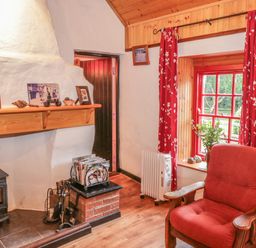 A living room with a wood stove fireplace a red armchair red curtains and a window with plants at Willowbrook Cottage in Askill County Leitrim