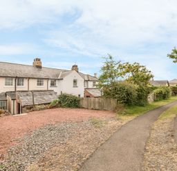 A row of white cottages with chimneys near a gravel area and a paved narrow road at Coastguard Cottage in Low Newton-by-the-Sea near Beadnell