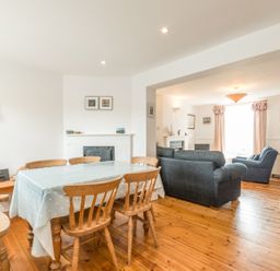 A dining area with wooden chairs and a table with a tablecloth next to a living room with sofas and a large window at Coastguard Cottage in Low Newton-by-the-Sea near Beadnell