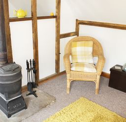 A corner of a room with a wood stove a wicker chair with cushions and a small table with a radio at The Hayloft in Necton near Swaffham