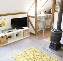 A living room with a television on a white stand a vase with flowers a wood stove and stools at The Hayloft in Necton near Swaffham