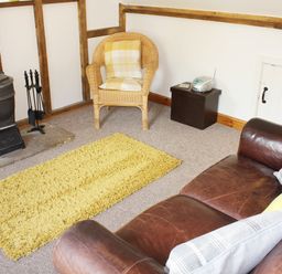 A living room with a wood-burning stove wicker chair yellow rug and leather sofa at The Hayloft Necton near Swaffham