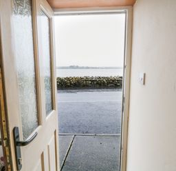 An open door showing a view of a road a stone wall and water beyond at Quayside House in Roundstone County Galway
