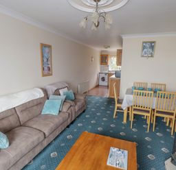 A living room with a beige sofa and blue cushions a wooden dining table with six chairs and a kitchen in the background at Quayside House in Roundstone County Galway