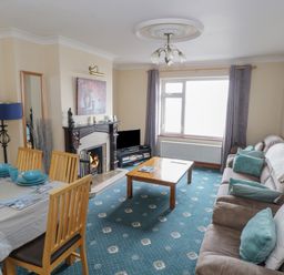 A living room with a dining table set with blue dishes a fireplace a flat screen tv and a sofa with pillows at Quayside House in Roundstone County Galway
