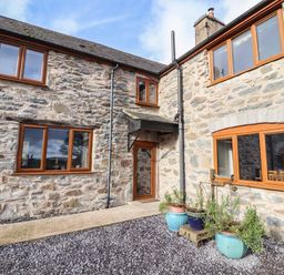 Stone exterior of a house with wooden framed windows a door and potted plants at Maestyddyn Farm House in Clawddnewydd near Ruthin