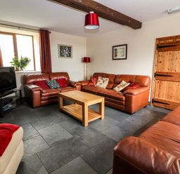 A living room with leather sofas a wooden coffee table a television and a wooden door at Maestyddyn Farm House in Clawddnewydd near Ruthin
