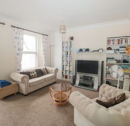 A living room with two beige sofas a round glass coffee table a television and bookshelves at Dunholme House in Teignmouth