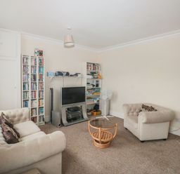 A living room with two beige sofas a glass top coffee table a television with bookshelves and a standing fan at Dunholme House in Teignmouth