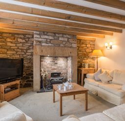 A living room with wooden beams a stone fireplace sofas a TV on a wooden stand and a wooden coffee table with cups at Fisherman's Cottage in Seahouses
