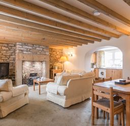 A living room with armchairs a sofa a wooden dining table and chairs a fireplace and a view into a kitchen at Fisherman's Cottage in Seahouses