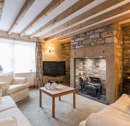 A living room with wooden beams on the ceiling a stone fireplace a wooden coffee table a television and cream sofas at Fisherman's Cottage in Seahouses