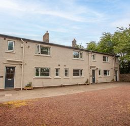 A two-story row house with multiple windows and doors in front of a gravel courtyard at Brians Cottage in Alnmouth