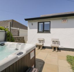 An outdoor patio area with a hot tub wooden chairs and a white building at Minerva in Trearddur Bay