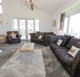 A living room with two patterned sofas a leather armchair a wooden coffee table and large windows at Minerva in Trearddur Bay